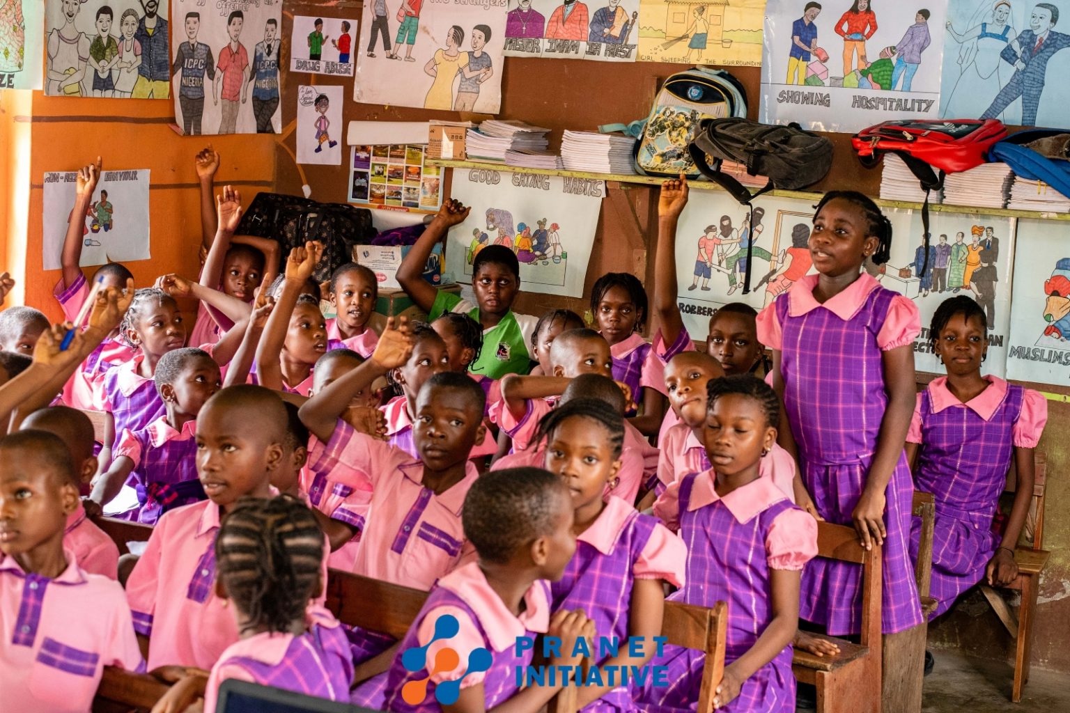 Pupils in pink and purple uniforms raising their hands in a classroom